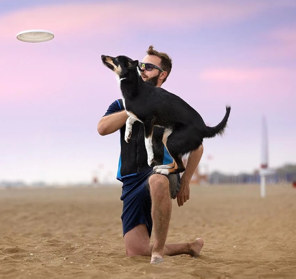Un educatore in spiaggia gioca a disc dog con un cane